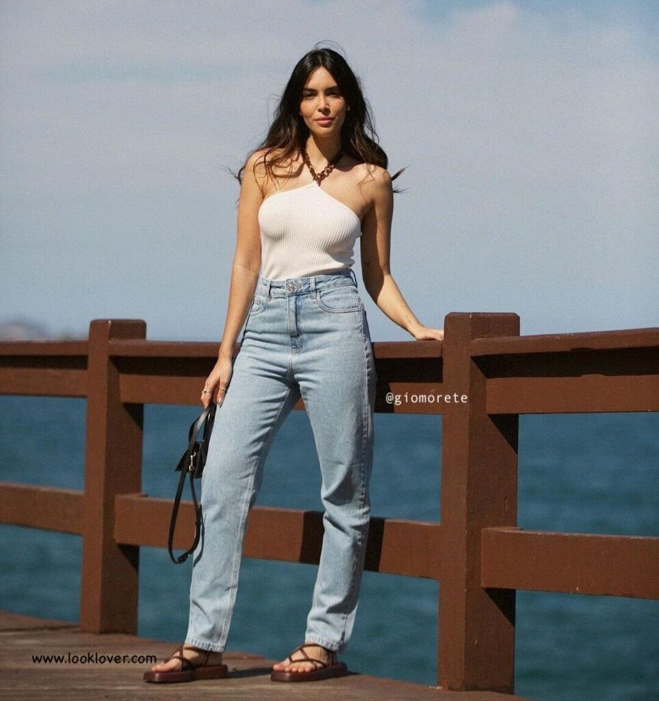 look confortavel de praia ou passeio durante o dia. Gio morete esta vestindo calça jeans, chinelo e uma blusinha com amarado no pescoço, bolsa pequena preta.